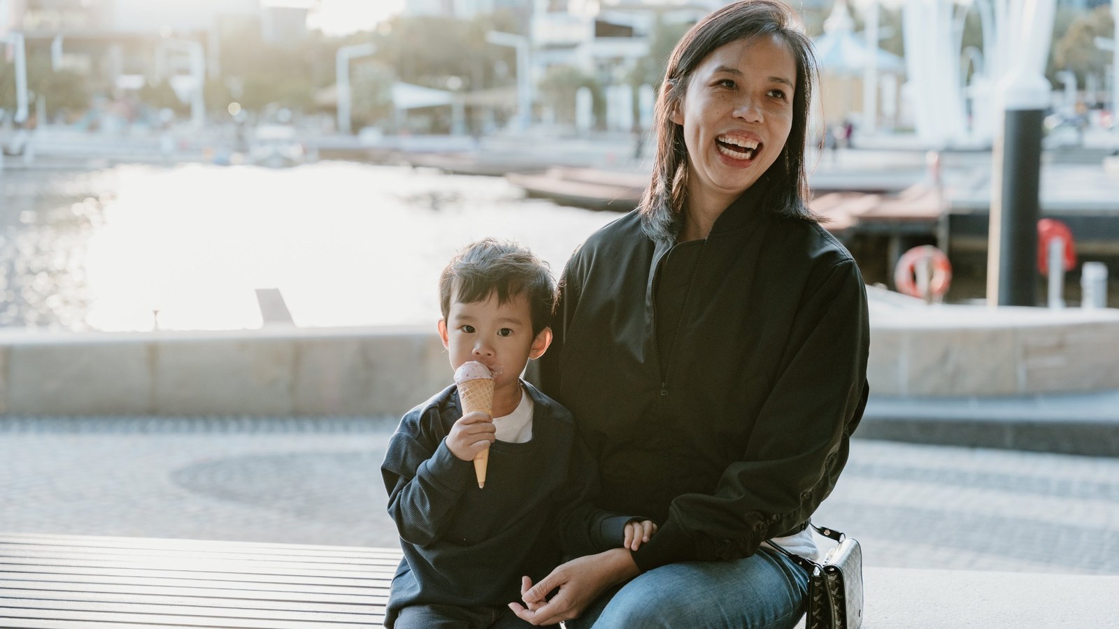 Joan laughing on a bench by the water while her son eats an ice cream cone